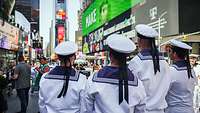 Sailorsin white uniforms stand in a square with large screen advertising spaces.