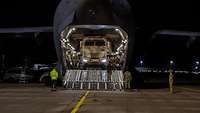 Transportflugzeug mit geöffneter Heckladeklappe, Militärfahrzeug auf Entladerampe. 