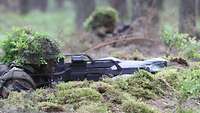 Soldaten liegen mit Waffen im Wald in einer Mulde