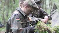 Zwei Soldaten bedeckt ihre Helme mit Naturmaterialien.
