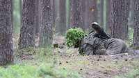 Eine Soldatin gleitet mit einer Panzerfaust auf dem Rücken über den Waldboden.