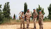 Vier Soldaten posieren mit Spitzhacke und zwei Schaufeln auf einem Hügel für ein Foto 