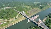 Luftaufnahme: Ein Containerschiff fährt unter einer Brücke hindurch.