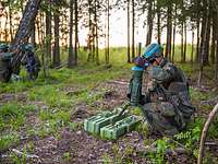 Der Soldat stellt im Wald eine Richtmine auf. Im Hintergrund knien weitere Soldaten.