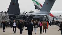 Viele Menschen laufen entlang militärischer und ziviler Großflugzeuge.