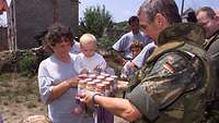 Ein Soldat verteilt in Rahmen humanitärer Hilfe Babynahrung an Einwohner im Kosovo-Einsatz