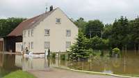 Ein Wohnhaus steht inmitten des Hochwassers, vor dem Eingang sind Sandsäcke gestapelt.