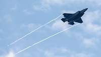 Ein Kampfjet bei leicht bewölktem Himmel zieht zwei Kondensstreifen hinter sich.