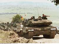 Mehrere Kampfpanzer fahren im Konvoi einen sandigen Schotterweg etlang
