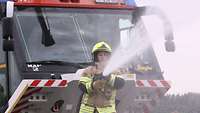 Eine junge Feuerwehrfrau spritzt mit einer Düse eine große Menge Wasser.