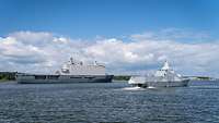 A gray Dutch dock landing ship and a Swedish corvette leave port.