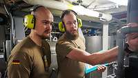 Zwei Soldaten mit gelben Gehörschutz stehen in einem Maschinenraum.