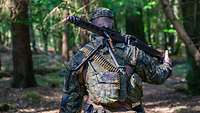 Rückenansicht: Ein Soldat mit einem MG3 auf der Schulter läuft durch den Wald.