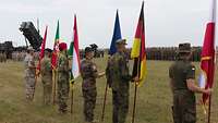 Unterschiedliche Soldaten stehen mit ihren Nationalfahnen vor einer militärischen Formation.