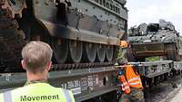 Ein Soldat mit Helm und Warnweste misst den Abstand der Ketten zum Rand der Bahnwaggons