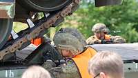 Ein Soldat mit Helm und Warnweste bringt einen Kettenkeil genau unterhalb der Laufrollen eines Pumas an