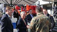 Eine Frau im Anzug unterhält sich vor dem Stand der Bundeswehr mit Karriereberatenden.