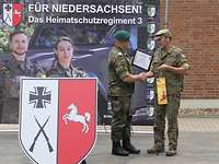 Ein Soldat übergibt einem anderen Soldaten eine Urkunde und ein Geschenk.