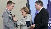 Angela Merkel befestigt das Ehrenkreuz der Bundeswehr für Tapferkeit an der Jacke eines Soldaten