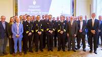 Eine Gruppe von Menschen in Uniform und Anzügen stehen nebeneinander für ein Gruppenfoto.