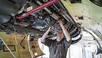 A soldier works on the fuselage of a fighter jet.