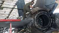 A soldier works on the engine of a fighter jet.