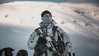 In den verschneiten Bergen posiert ein deutscher Soldat in Schneetarnfleck mit Gewehr.