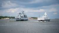 Zwei kleine graue Kriegsschiffe fahren nebeneinander in einem Hafengebiet
