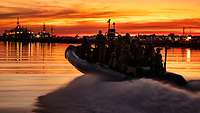 Ein Festrumpfschlauchboot mit mehreren Soldaten bei voller Fahrt im Hafen bei Sonnenuntergang.