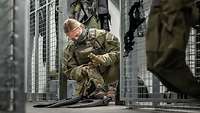 Eine Soldatin hockt in einem vergitterten Raum und bereitet ihre Ausrüstung vor