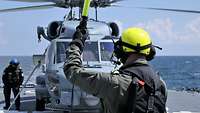 Ein grauer Hubschrauber auf dem Flugdeck eines Kriegsschiffs. 
