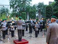 Viele Musikerinnen und Musiker in Uniform spielen auf ihren Instrumenten, vorn der Dirigent