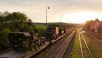 Bundeswehrfahrzeuge stehen auf Eisenbahnwaggons bei Sonnenuntergang
