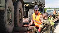 Ein Soldat unterhält sich an einem mit Fahrzeugen beladenen Waggon mit einem weiteren Soldaten