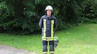 Ein Mann in Feuerwehruniform steht am Rand eines Weges vor Bäumen.