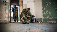 Zwei Soldaten in ABC- Schutzausstattung prüfen das Gebäudeinnere auf Kampfstoffe