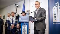 Minister Pistorius am Pult, spricht zu festlich aussehenden jüdischen Rabbinern in blauer Robe und Hut