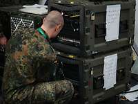 Ein Soldat arbeitet an Server-Einheiten, die in olivgrünen Transportboxen installiert sind
