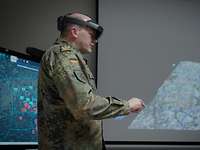 Ein Soldat mit VR-Brille steht vor einem Monitor und einer Leinwand mit Projektion