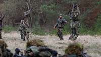 Soldaten werden auf einer Wiese vor einem Waldstück militärisch gedrillt