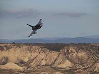 Ein Eurofighter fliegt über einer karge Landschaft eine Rechtskurve.