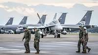 American Navy maintenance personnel walk in front of a fighter jet.