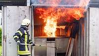 Eine Feuerfrau vor einem Container, in dem ein Topf auf dem Herd explodiert