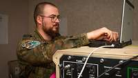 A soldier standing at a laptop and an IT platform.