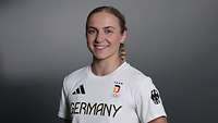 Eine junge Frau posiert in einem weißen Sporttrikot mit dem Schriftzug "Germany" lächelnd für ein Foto