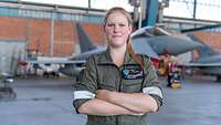 Eine junge Frau im Overall steht vor einem Flugzeug der Bundeswehr und schaut in die Kamera.