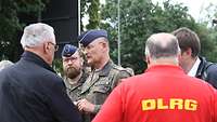 Ein Soldat spricht zu einem Zivilisten, ein weiterer Soldat und ein Mann in "DLRG"-Shirt hören zu.