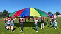 Menschen lassen ein in Regenbogenfarben gehaltenes Schwungtuch in die Luft fliegen