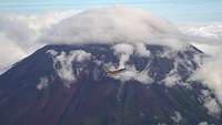 A wrapped combat aircraft in front of a mountain chain covered in clouds.