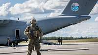 Ein Soldat steht auf einer Start- und Landebahn vor einem Flugzeug.